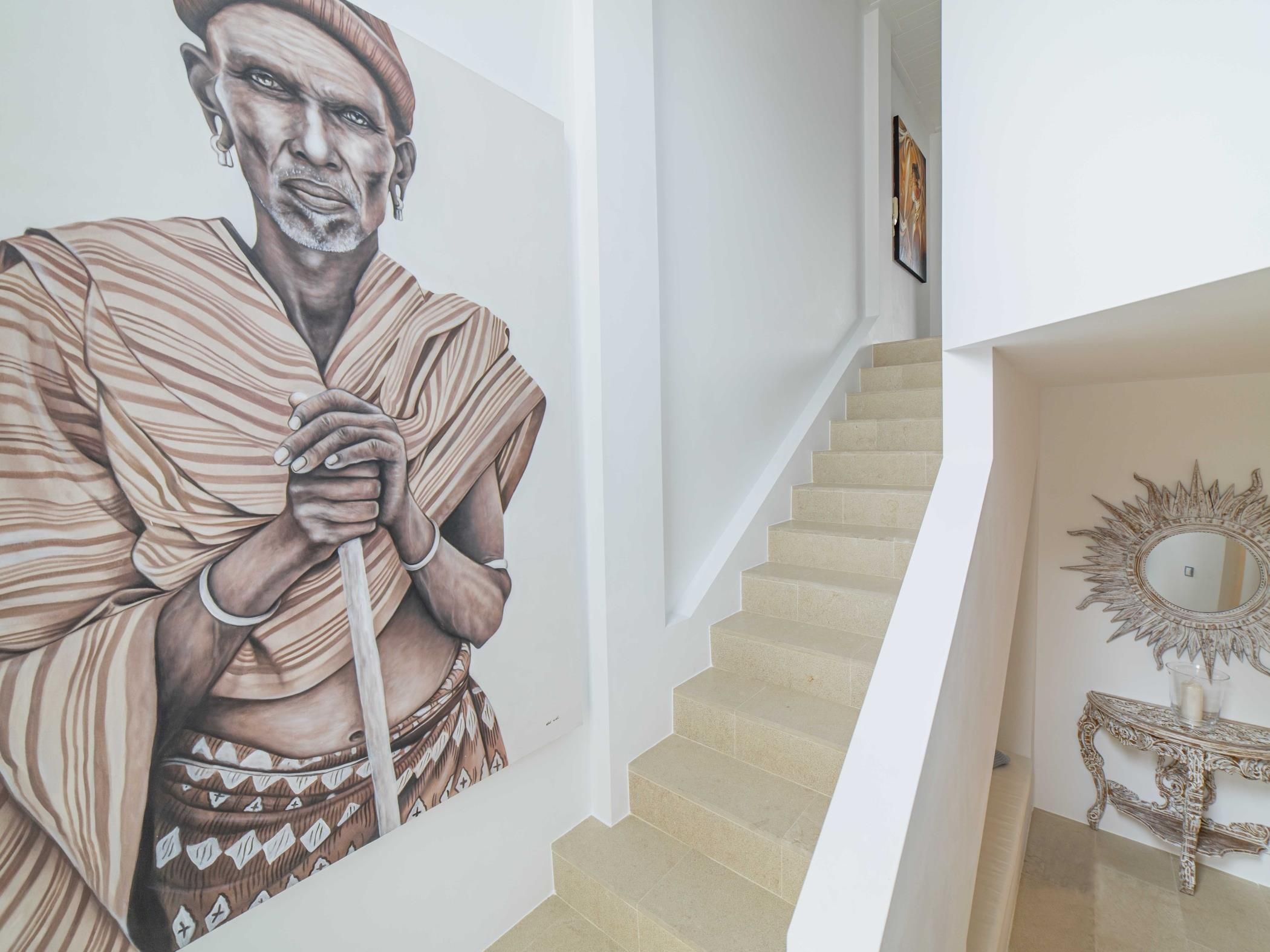 A staircase with a handrail, a wall with a large mural, and a decorative mirror on the lower landing.