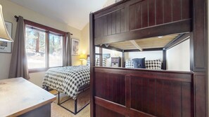 Una habitación con cama, escritorio, ventana con cortinas y vista a árboles.