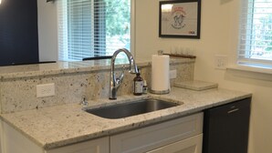 Een keuken met een granieten aanrecht, een roestvrijstalen spoelbak, witte kastjes, een zwarte vaatwasser, een klok en een ingelijst certificaat aan de muur.