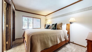 A bedroom with a bed, two bedside lamps, a window with blinds, and a door.