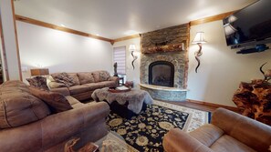 A cozy living room with a fireplace, a sofa set, and a flat-screen TV mounted on the wall.