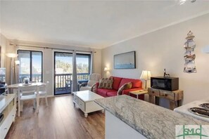 Relax in this stylish living area with a sofa, coffee table, and TV, leading to an outdoor space with a tree-lined view.
