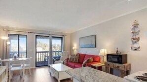 A room with a red sofa, a white table, a TV on a wooden stand, and a balcony with a view of the sea. - Tybee Beach views, just steps to the ocean (Tybee Island)