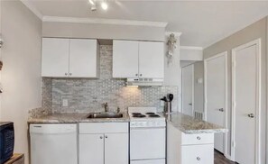 A modern kitchen with white cabinetry, a granite countertop, a dishwasher, and a stove.