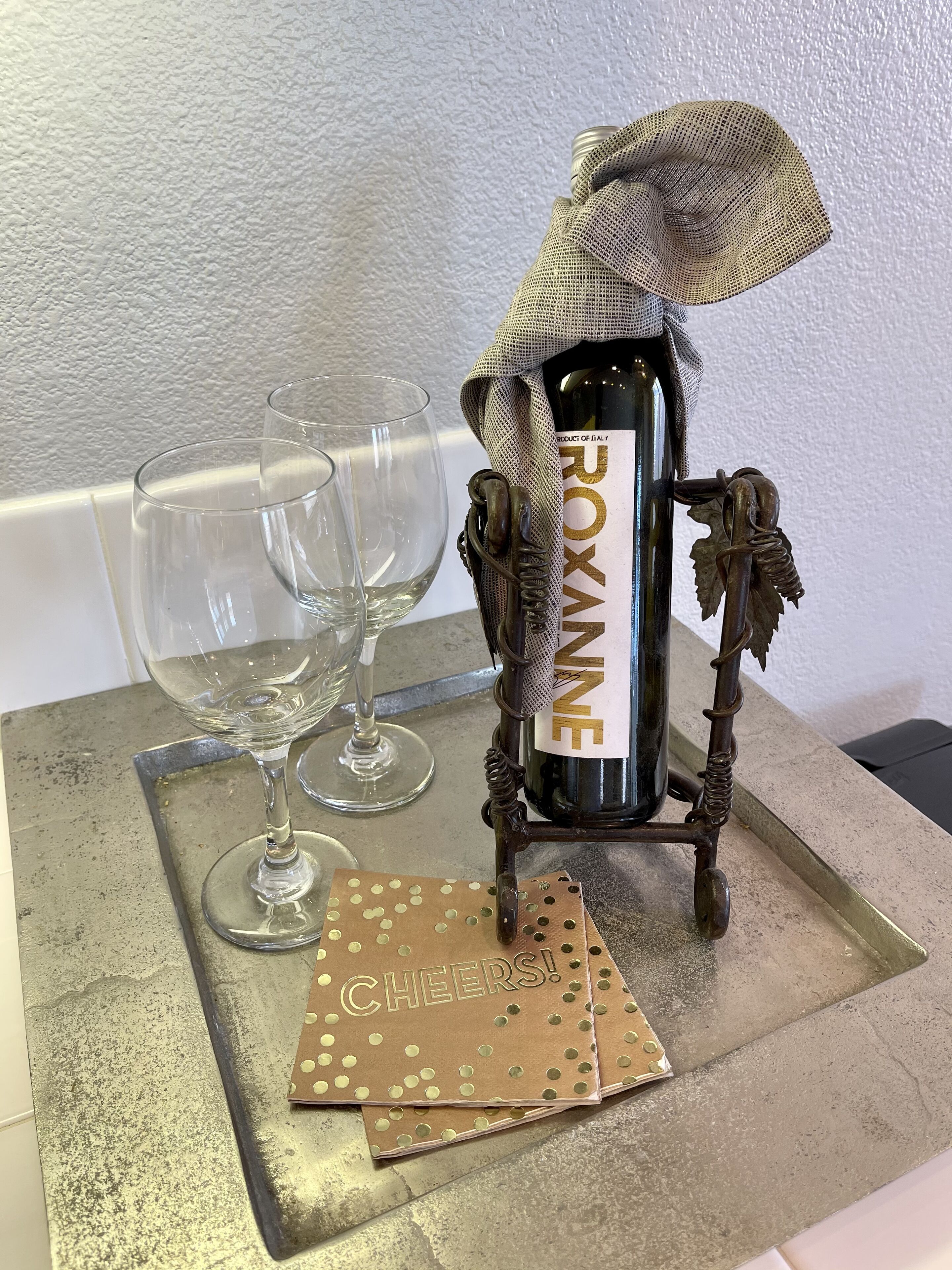 Una botella de vino con etiqueta, dos copas de vino vacías y un pequeño adorno sobre una bandeja.