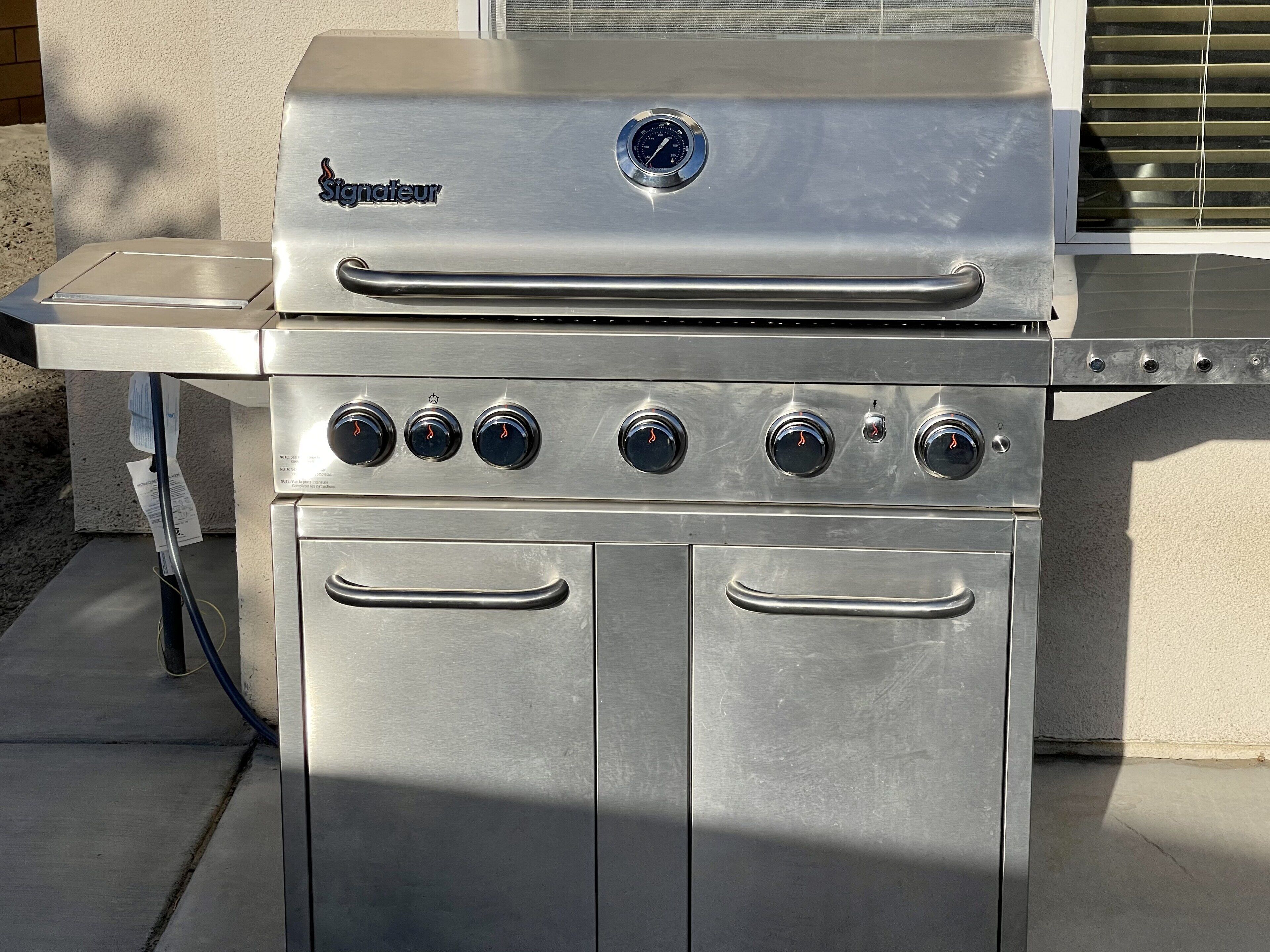 A stainless steel outdoor grill with four burners, a control panel, and a side burner.