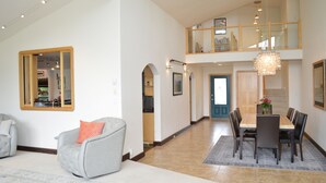 A spacious living area with a dining table, chairs, and a comfortable armchair. A large mirror and a chandelier are visible. - Gorgeous Modern Alaskan Home with Ocean /Mt View 10 minute walk to sandy beach (Kenai)