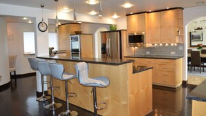 A modern kitchen with a central island, stainless steel appliances, and bar stools. - Gorgeous Modern Alaskan Home with Ocean /Mt View 10 minute walk to sandy beach (Kenai)