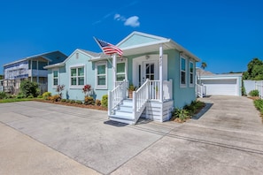 A light blue house with a white porch and a small American flag.