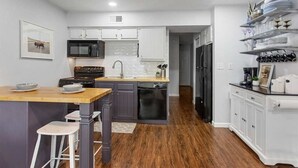 Una cucina moderna con isola in legno, mobili bianchi e lavastoviglie nera.