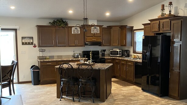 Una cocina moderna con armarios de madera, una isla central con taburetes de bar, un refrigerador negro y un microondas.