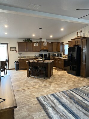 A modern kitchen with wooden cabinets, a central island with bar stools, a black refrigerator, and a microwave.