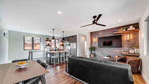 A modern kitchen with a central island, bar seating, and a TV mounted on a brick wall.