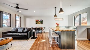 A modern kitchen with a central island, a dining area with a black leather sofa, and a bar area with a view of the mountains.