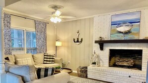 Un salon doté d’une cheminée, de rideaux à motifs et d’un ventilateur de plafond.