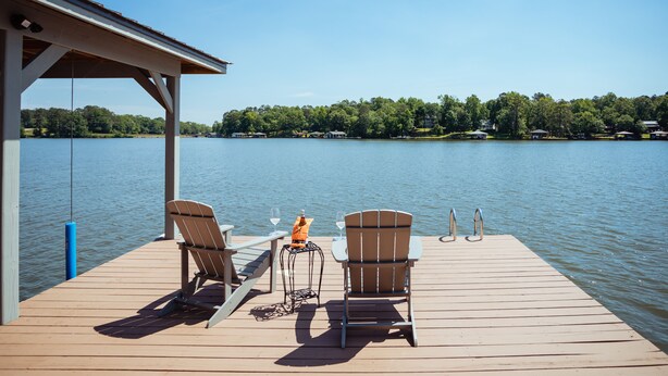 Une jetée en bois avec deux fauteuils Adirondack, une petite table avec une bouteille et un verre, et une canne à pêche.