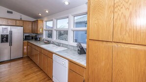 Una cocina con armarios de madera, lavavajillas, refrigerador, microondas y ventana con vistas al exterior.