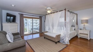 Un dormitorio con cama con dosel, un televisor sobre un tocador, un sofá y un balcón con vistas.