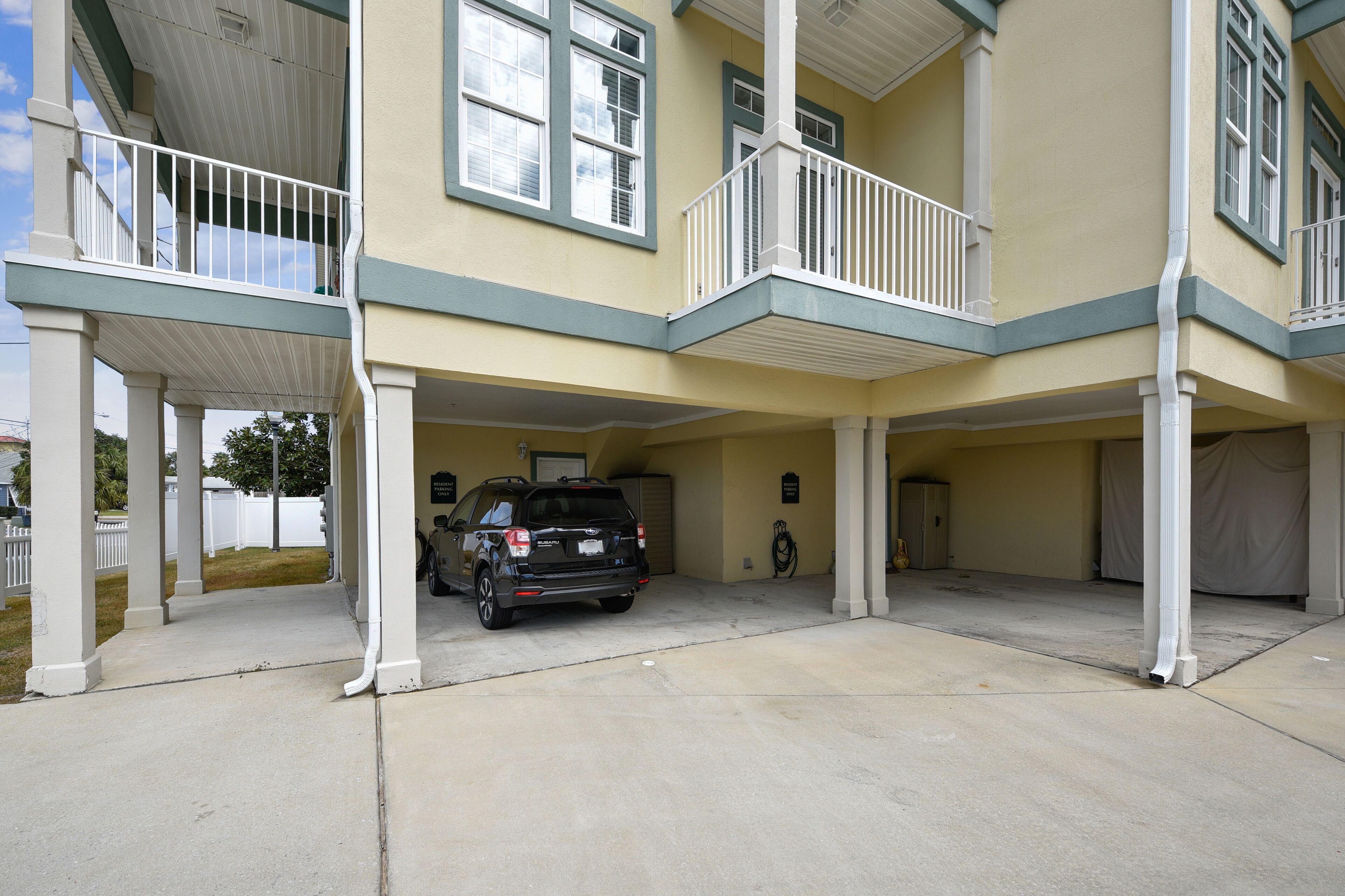 A two-story building with a covered parking area, a black SUV parked in the middle, and a person walking near the entrance.