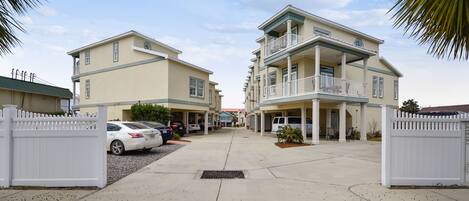 A residential building with a central entrance, multiple balconies, and a gated driveway.
