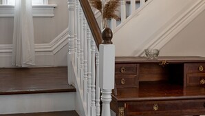 Un escalier avec des balustrades blanches et une main courante en bois, menant à un palier où se trouvent un bureau en bois foncé et un vase rempli d’herbe de la pampa séchée.