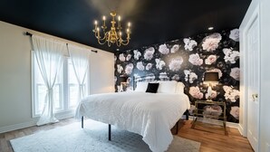 Une chambre à coucher avec un grand lit, un lustre, un papier peint à motifs floraux et une table de chevet avec une lampe.