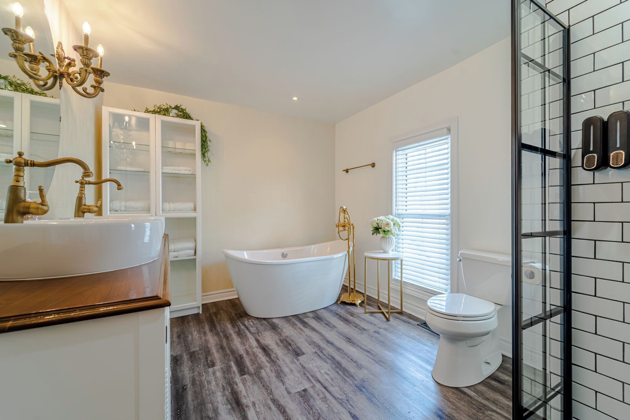 A bathroom with a freestanding bathtub, a white toilet, a vanity with a gold faucet, and a glass shower enclosure.