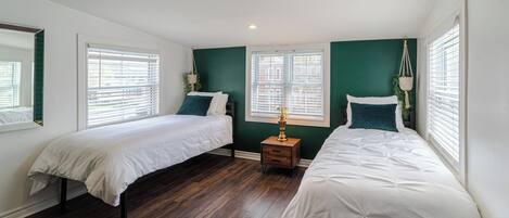 A bedroom with two beds, a nightstand, and a window with blinds.