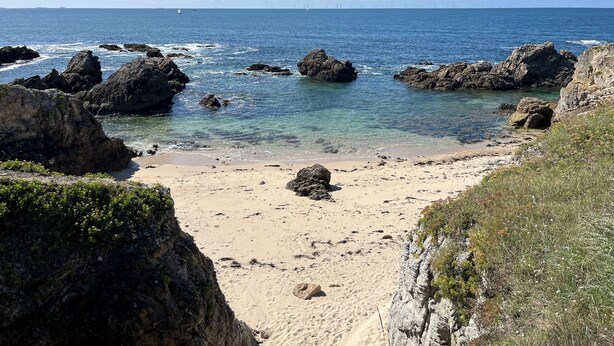 Ein Küstenstrand mit Felsformationen und klarem, blauem Wasser.