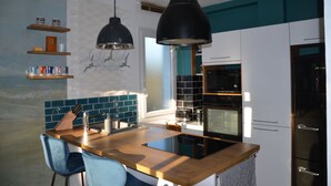 Eine moderne Küche mit einer Holzinsel, schwarzen Pendelleuchten, Türkis-Weiß-Schränken und einem eingebauten Backofen.