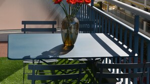 Ein Balkon mit Tisch und Stühlen, einer Blumenvase und Blick auf Strand und Meer.