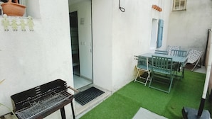 Eine Terrasse mit Grill, Tisch und Stühlen sowie einem Bereich mit grünem Kunstrasen.
