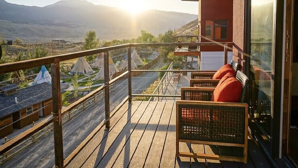 Un balcón con sillones de mimbre, una terraza de madera y vistas a montañas y un valle.