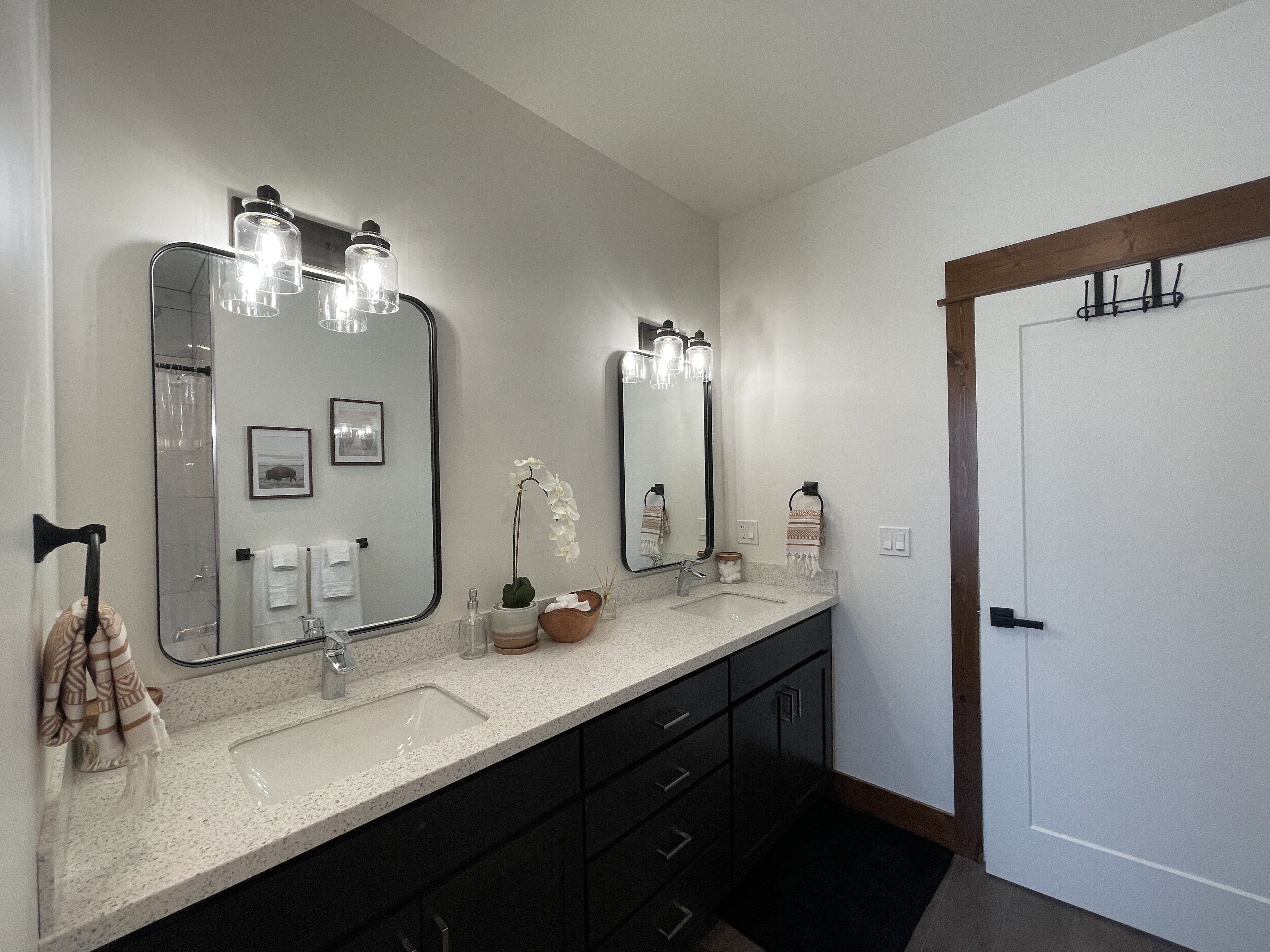 A bathroom with two sinks, a large mirror, and a door with a coat rack.
