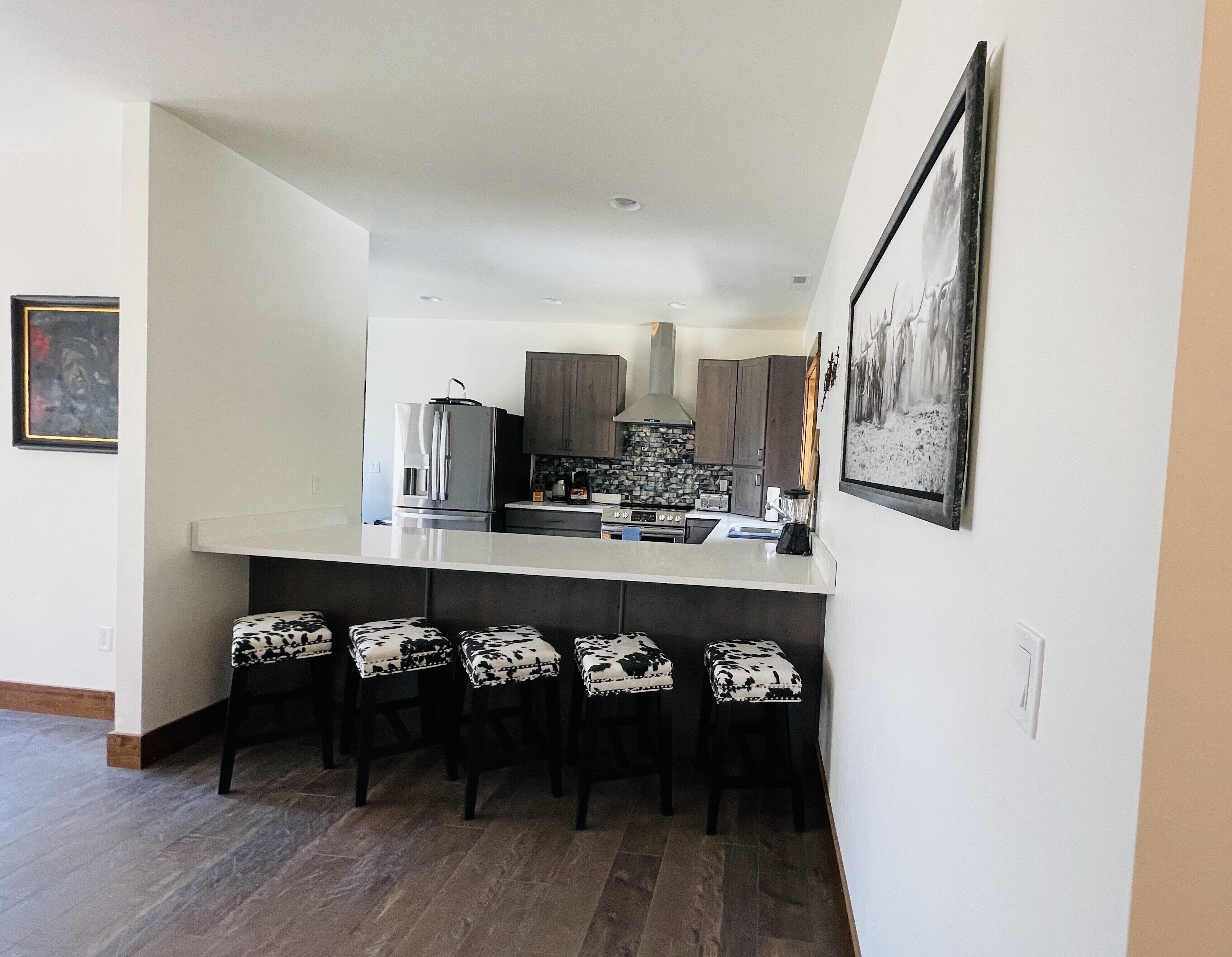 A modern kitchen with a central island, bar stools, and a large framed picture on the wall.