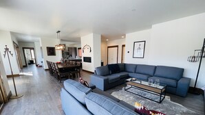 Un amplio espacio de estar con un sofá modular grande, una mesa de comedor y una cocina al fondo.