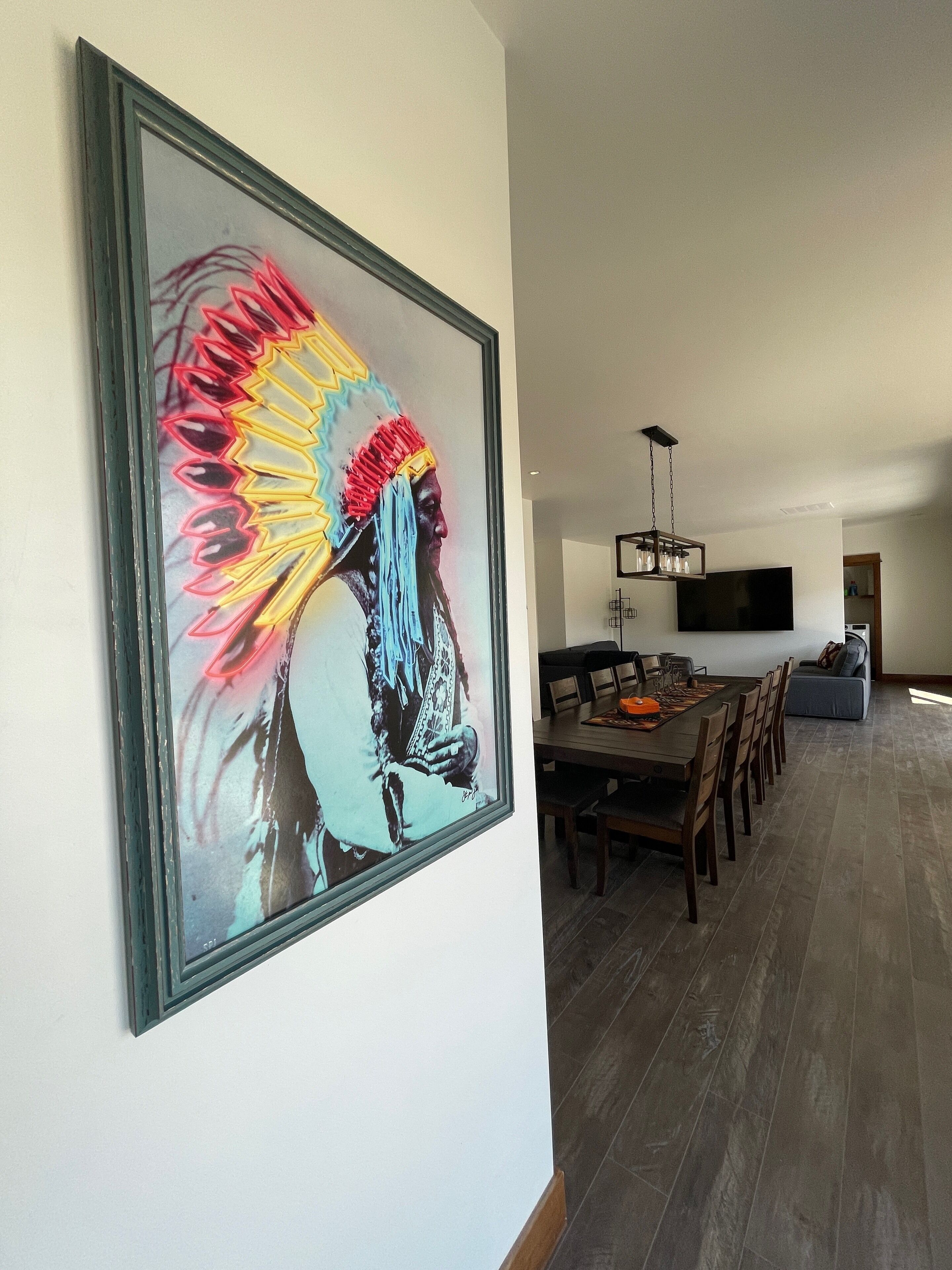 Un comedor con una larga mesa de madera y sillas, una araña y una gran obra de arte enmarcada en la pared.
