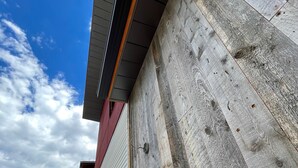 Un edificio con techo inclinado, pared exterior de madera y sección de revestimiento metálico.