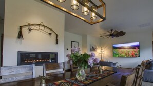Un comedor con una mesa de madera larga, un adorno en la pared, una chimenea y un televisor montado.