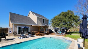 A residential swimming pool with a wooden deck, lounge chairs, and umbrellas.