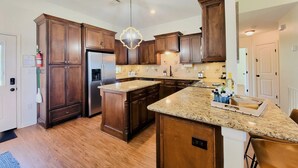 A spacious kitchen with dark wood cabinets, a stainless steel refrigerator, granite countertops, and a central island.