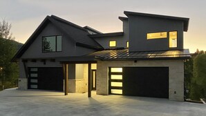 A modern two-story house with a garage, large windows, and a sloped roof. - New Family-Friendly Home Overlooking Fox Creek, Large Deck & Cozy Furnishings (Steamboat Springs)