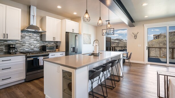 A modern kitchen with white cabinets, a large island with bar stools, a stainless steel range, and a stone backsplash. - New Family-Friendly Home Overlooking Fox Creek, Large Deck & Cozy Furnishings (Steamboat Springs)