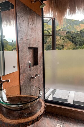 Bathroom features a large glass sink, stone tiles, and a window with a view of the surrounding hills.