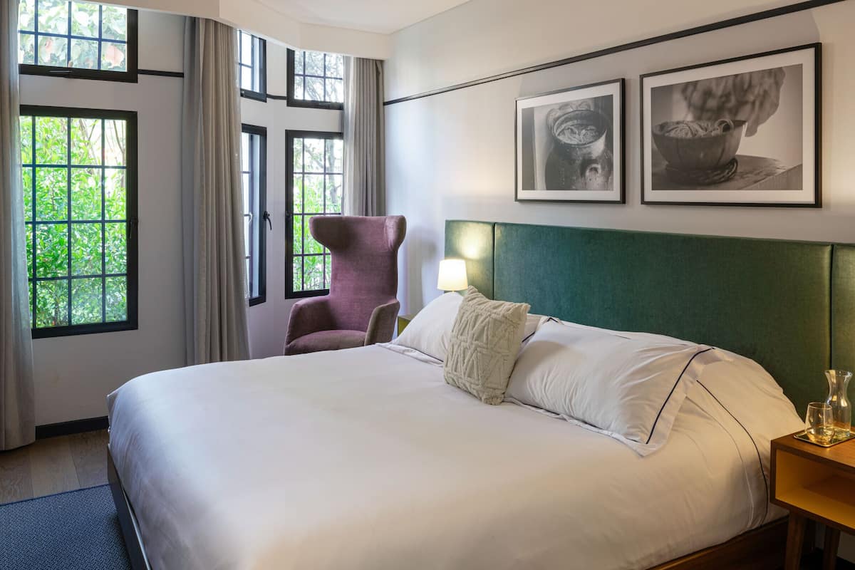 A hotel room with a large bed, two bedside lamps, a chair, and two framed pictures on the wall.