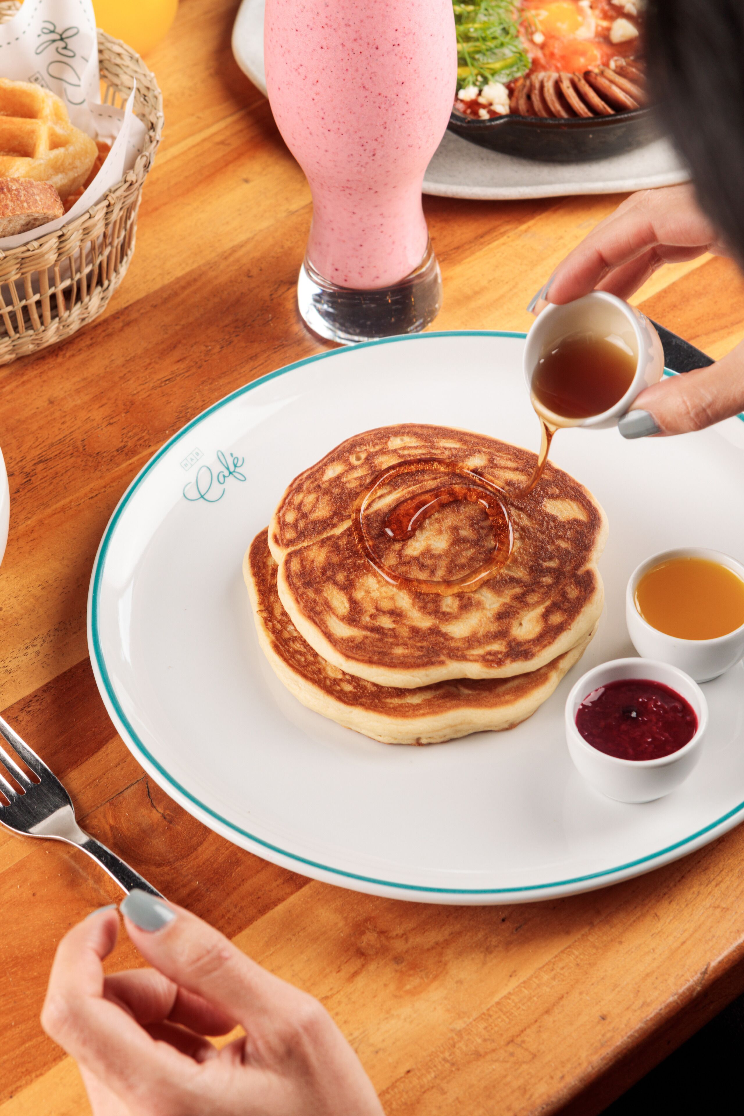 A plate of pancakes with syrup and two small bowls of jam on a wooden table.