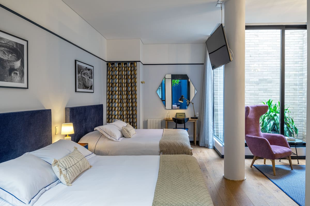 A modern hotel room with two beds, a desk, a chair, and a TV.