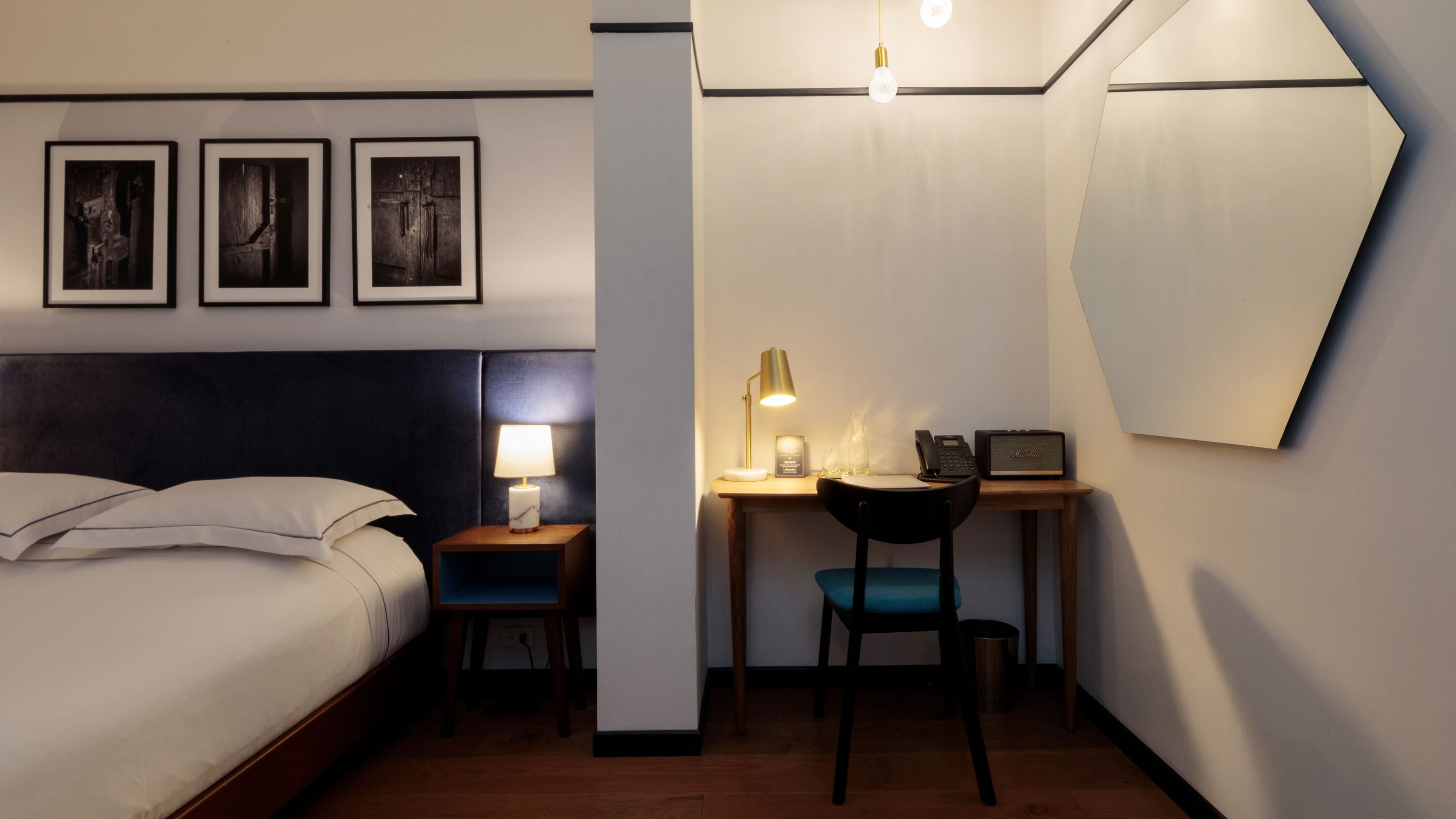A hotel room with a bed, a desk with a lamp, a chair, and a telephone.