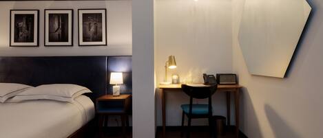 A hotel room with a bed, a desk with a lamp, a chair, and a telephone.
