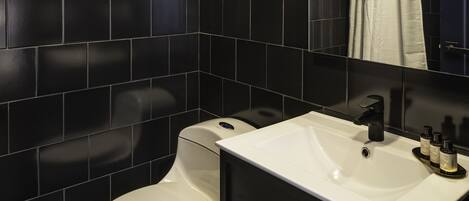A modern bathroom with black tiled walls, a white toilet, and a sink with a mirror above it.